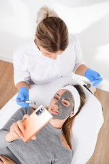 Face mask for a woman in a gray sweater with a mobile in hand, lying on a salon couch