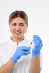 Smiling doctor in white overalls and blue rubber gloves draws cosmetics in a syringe