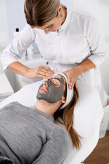 Specialist in the beauty field makes a face mask for a girl with light hair in a beauty salon