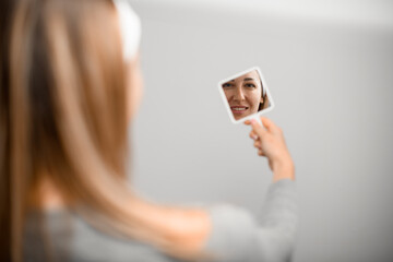 Mirror in the hand of a woman with fair skin who is reflected in it on a white background