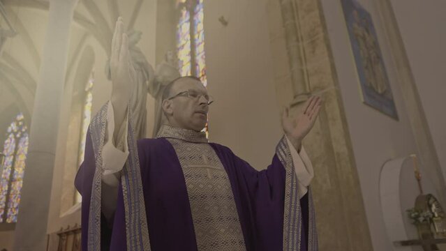 Mid adult caucasian christian priest in purple robe preaching and crossing in church. Clergyman standing on podium in cathedral during Holy Mass medium shot