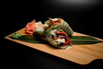 Stuffed rolls with vegetables, seafood and meat on a green leaf on a black background
