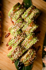 Top view of sushi with sesame and sauce on a long green leaf