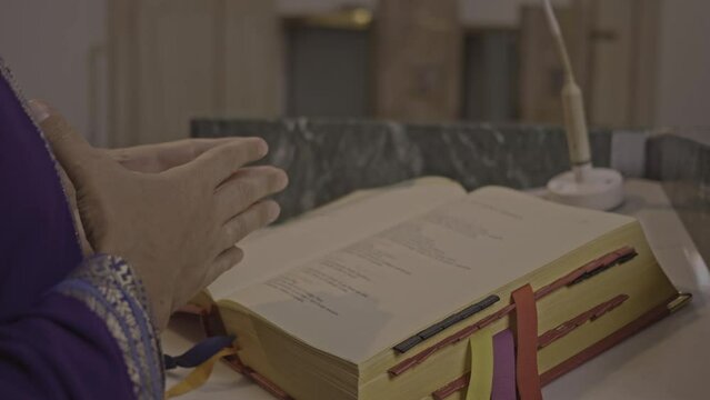 Christian priest preaching psalmbook in church during Holy Mass close up. Pastor standing on podium in Catholic cathedral, reading Bible and praying close view