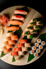 Sets of sushi and rolls on a large round light wood stand on a dark background - 791712047
