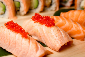 Appetizing rolls wrapped in salmon and fillet with red caviar on a wooden board - 791713498