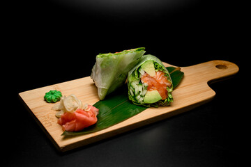 Rolls with salmon, salad leaf and cucumbers on a thick light wood stand with a ginger and wasabi - 791714299