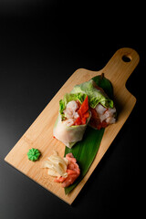 Wrapped in leaf rolls with vegetables and seafood on a wooden board on a black background