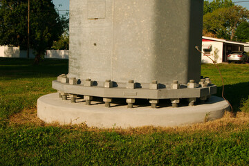 Close up over green grass low wide horizontal of a steel power pole base screws with concrete base...
