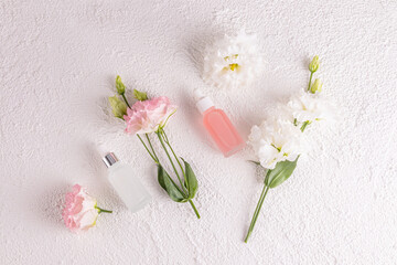 Two matte cosmetic bottles with a dropper with a natural skin care product for face on a white background among delicate spring flowers. Flat lay