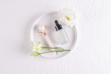 Cosmetic Matte Bottle With Dropper With Natural Massage Product, Oil Or Serum On White Ceramic Plate With Flowers And Stone Roller Massager. Spa