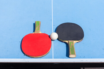 Red and black Table Tennis Paddles and ball on the blue table tennis table with net. Ping Pong...