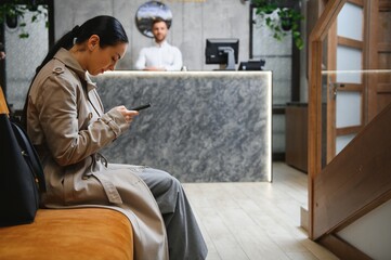 Businesswoman with luggage in modern hotel lobby using smartphone - Powered by Adobe