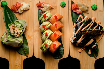 Three sets of rolls and sushi on a wooden boards with green leaf with ginger and hot sauce
