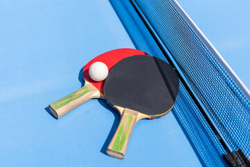 Two table tennis or ping pong rackets and ball on blue table with net