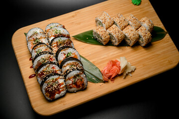 Sets of sushi on a wood stand with pickled ginger and hot wasabi on a black background