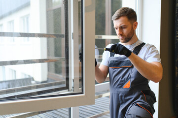 Workman in overalls installing or adjusting plastic windows in the living room at home