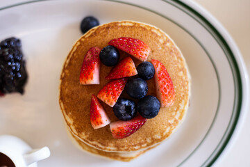 Large cheese pie topped with strawberries and blueberries. Surrounding elements include jam, honey jars, and butter at the end, which looks delicious.