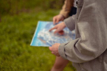A close-up of hands holding a map. A boy and a girl lost in the woods, engaging in orienteering....
