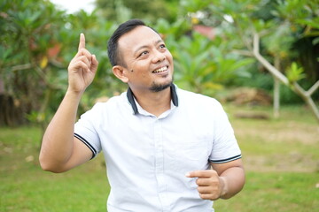 Asian male model wearing white shirt is sitting with facial expression in nature