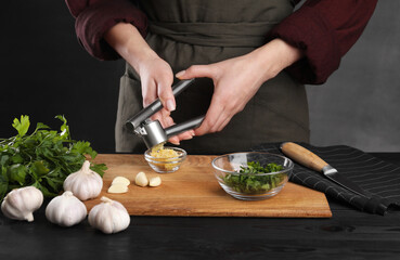 Woman squeezing garlic with press at black wooden table, closeup