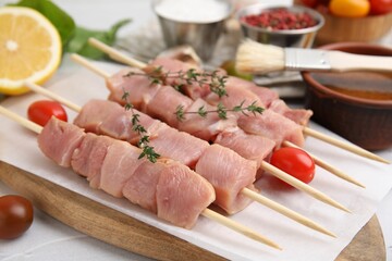 Skewers with cut raw meat, thyme and tomatoes on table, closeup