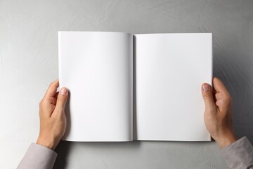 Man holding blank book at light grey table, top view. Mockup for design