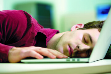 Sleepy man rests head on desk, overwhelmed at work
