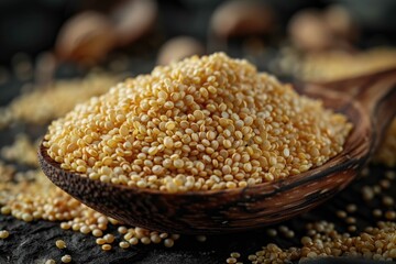 A wooden spoon is filled with a pile of golden quinoa seeds, spilled on a dark table.