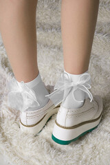 Close-up of a woman's legs wearing white socks with bows and sneakers. The girl is standing on a...