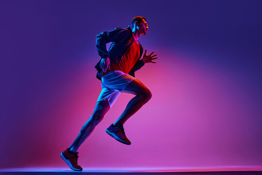 Active young man, athlete in sportswear in motion training, running on gradient pink purple background in neon light. Concept of active and healthy lifestyle, sport, hobby, motivation, endurance