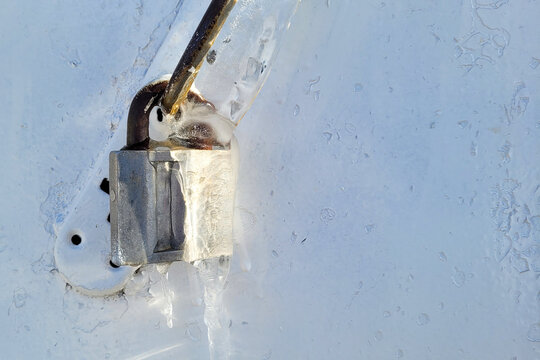 External padlock front door under a thick layer of ice, winter ice icicle on the lock.