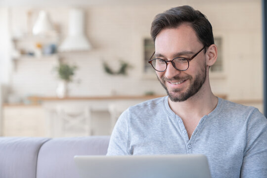 Successful confident young adult businessman using laptop for checking e-mail, searching web, online shopping, working, e-learning, watching movie and webinars at home indoors