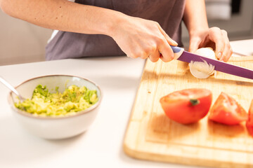 A woman is cutting a tomato on a wooden cutting board