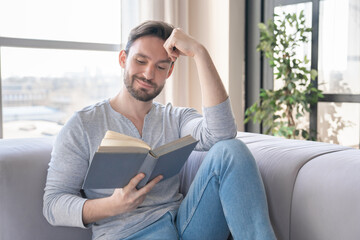 Excited relaxed young caucasian man reading a book, e-learning, having a break chilling after work...