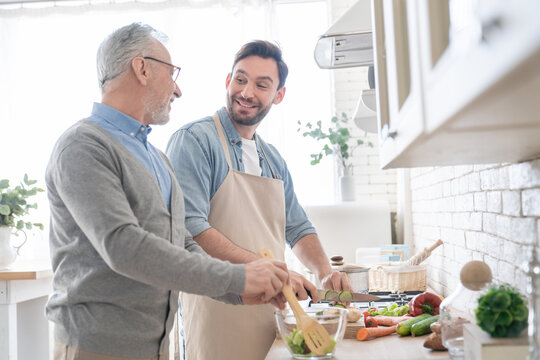 Happy young caucasian son talking with his old elderly senior father while cooking dinner, lunch in the kitchen. Preparing food meal together. Happy father`s day! I love you, dad! Men cooking together