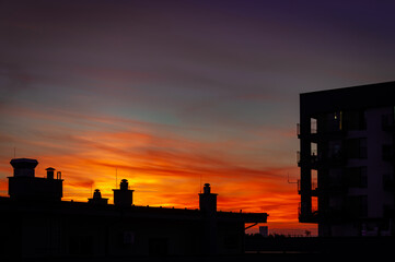 sylwetka budynków na tle zachodzącego słońca, czarne kształty, pomarańczowe niebo, 