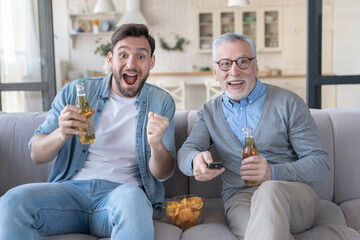 Cheerful energetic excited football soccer baseball fans old father and adult son rooting cheering...