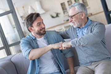Old elderly senior father together with his young adult son doing fists gesture, giving fists...
