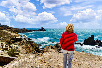 Blonde woman with curly hair looking at the horizon at the Las Sirenas reef in Cabo de Gata-Níjar, Almería, Spain