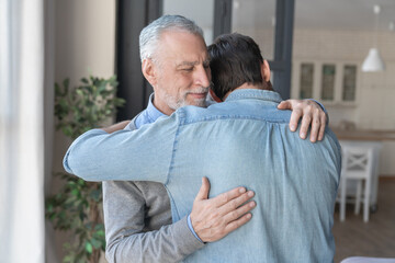 Loving cute old elderly senior father hugging embracing his young adult son showing him love and...
