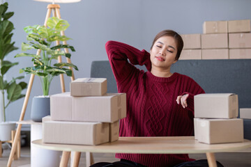 A small SME business owner feels tired while sitting on his home desk packing products into boxes.