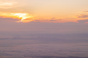 View of sunrise over white puffy clouds on horizon.