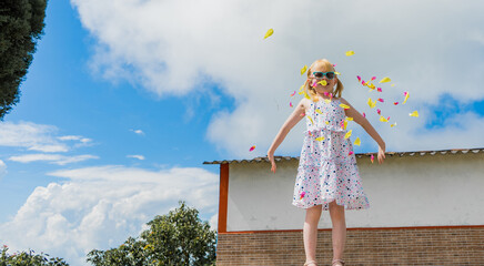niña albina usando un vestido y jugando en el patio de su casa con petalos de flores 