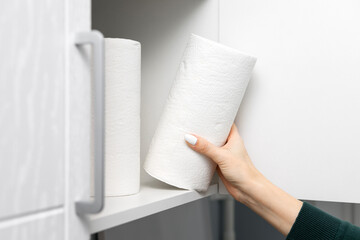 housewife takes out a roll of paper towel from the kitchen cabinet.