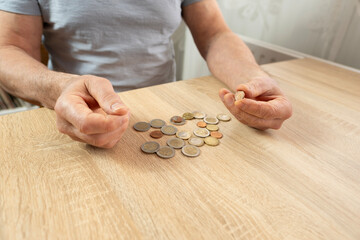 poor pensioner lays out euro cent coins on wooden table, counts meager cash money on table,...