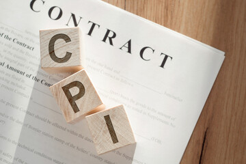 Acronym CPI made with wood building blocks on a wooden table with contract documents.