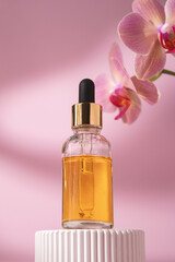 Cosmetic glass bottle with dropper for essential oils and serum on a podium with orchid flower. Face and body care spa concept and natural cosmetics