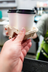 Person holding two takeaway coffee cups in a carrier, illustrating the culture of coffee on-the-go