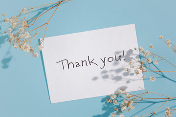 Handwritten message on azure paper with a backdrop of blue skies and twigs. The rectangle card with a plant on the slope in elegant font
